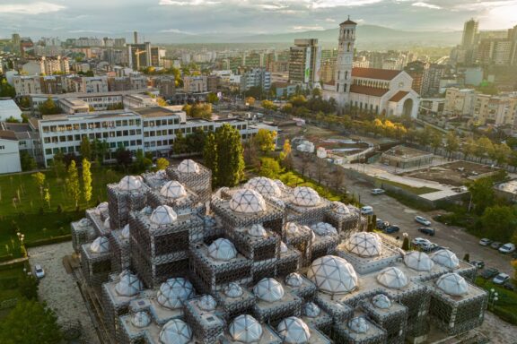 Aerial view of Pristina, Kosovo highlights the unique dome architecture of the National Library, amidst the cityscape in daylight.