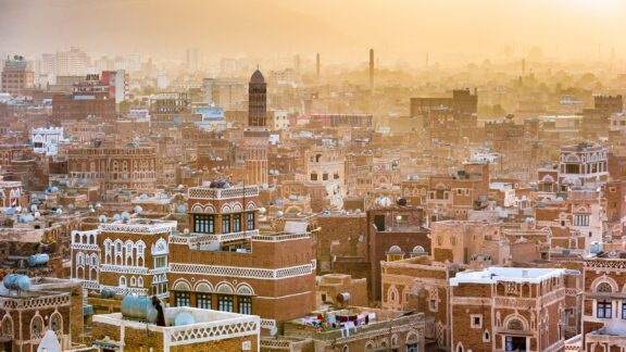 A panoramic view of Sanaa, Yemen displays dense, traditional buildings with unique architecture under a hazy sky.