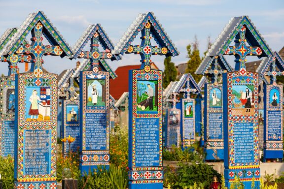 A colorful cemetery with ornate, vividly painted crosses featuring traditional patterns and illustrations, located in Romania.