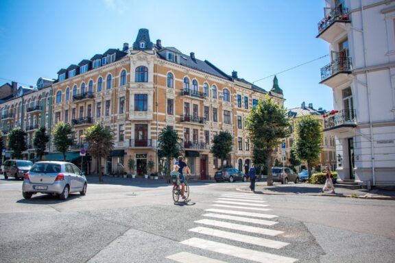 A sunny day in Oslo, Norway, with a view of a street featuring classic European architecture and a cyclist crossing the road.