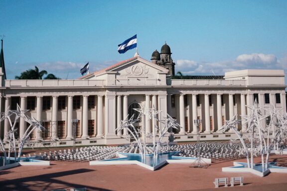 Nicaragua's National Palace features a neoclassical facade, multiple flags including its own, and a foreground fountain.