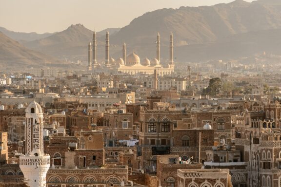 Sana'a, Yemen's old town showcases ancient architecture, unique window designs, a grand mosque with minarets, set against mountainous backdrop.