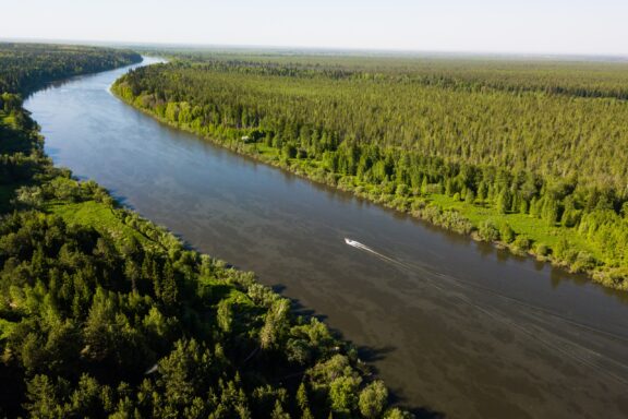 Boat sails along the river. Ob river flows through the taiga. River landscape, beautiful sky reflection in water. Vasyugan Swamp from aerial view. Tomsk region, Siberia, Russia