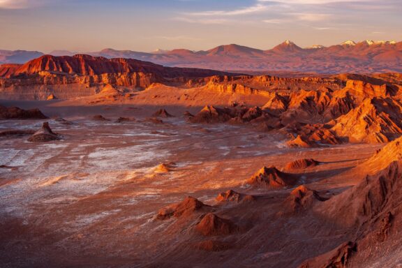 A dusk landscape with rugged terrain, a central salt deposit resembling a moon crater, and mountains under a glowing sky.