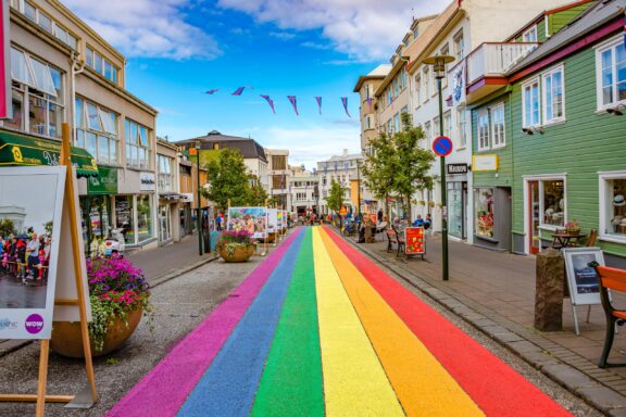 A vibrant street in Reykjavik, Iceland, with a rainbow-colored crosswalk, colorful buildings, and pedestrians.