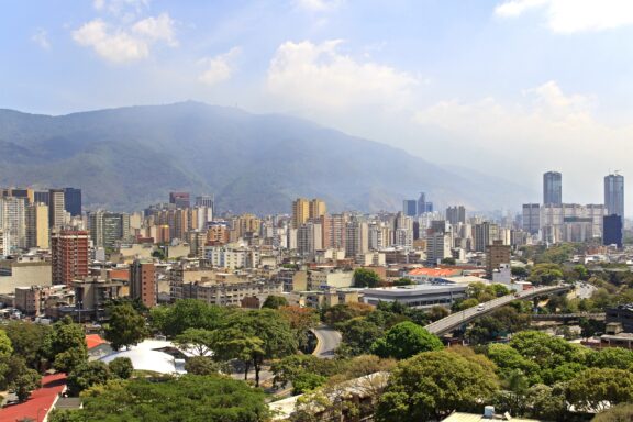 Caracas' skyline features a blend of high-rises and residences, set against green mountains and a blue sky.