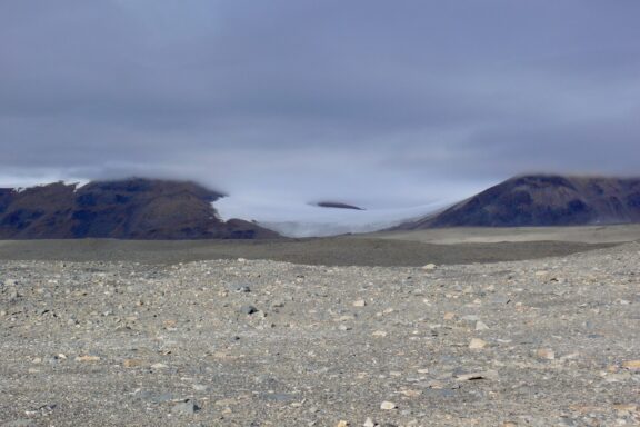 A view of the Taylor Dry Valley with a rocky foreground and distant mountains partially shrouded by clouds.