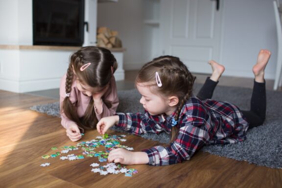 Two Children Playing with Puzzle Pieces on Floor Children playing puzzles at home