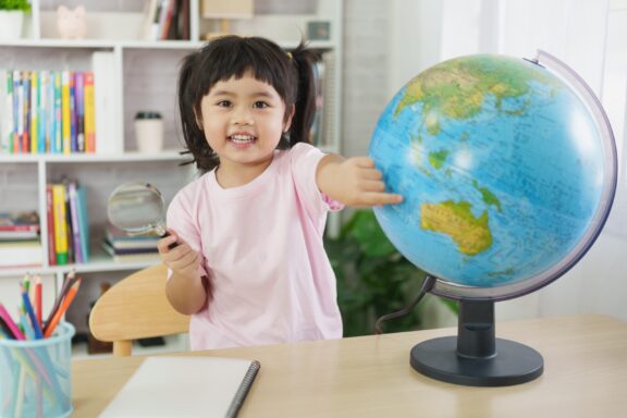 Asian cute girl smiling observing and point finger at educational globe.