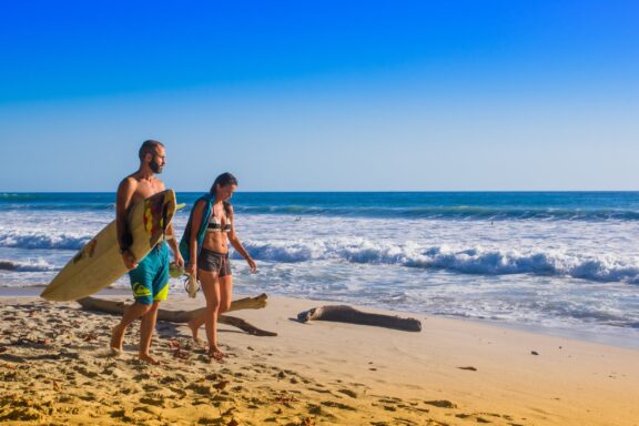 Santa Teresa, Costa Rica - June, 28, 2018: Couple of surfers on the beach of Santa Teresa walking and enjoying the time together in a beautiful sunny day with blue sky and blue water in Costa Rica.