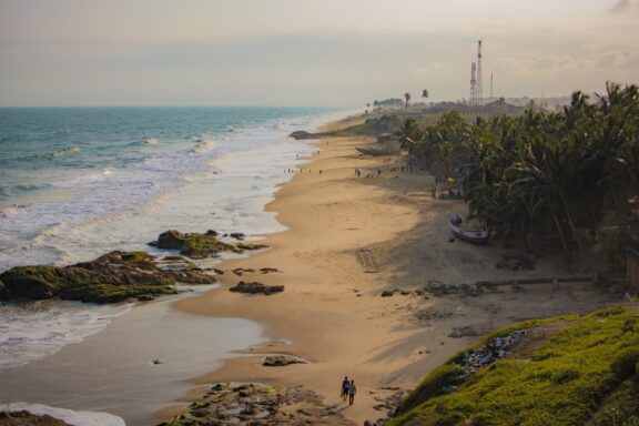 Cape coast in Ghana, palm trees and people walking on the beach.