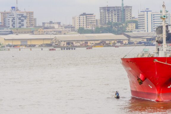 a beautiful view of a canoeist paddling near a ship at the Bonaberi quay with the city of Douala in the background.