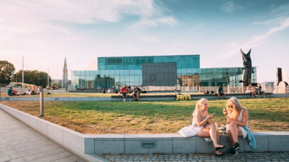 Two Women Sitting and Enjoying the Sun in a City Square young women People are relaxing in front of the Kiasma museum and Sanoma building in Helsinki, Finland.