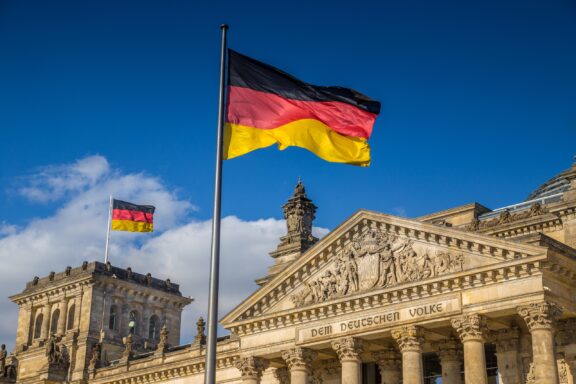 German flags waving in the wind at famous Reichstag building, seat of the German Parliament (Deutscher Bundestag), on a sunny day with blue sky and clouds, central Berlin Mitte district, Germany.