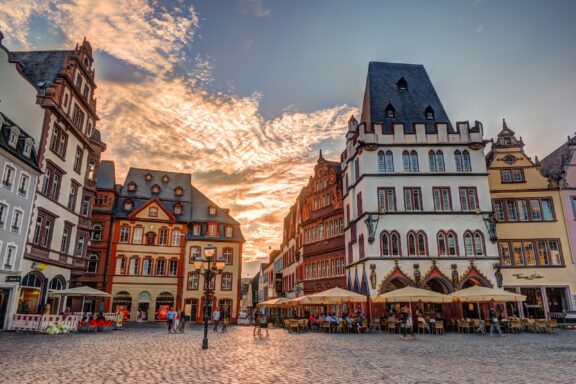 People walk under a sunset sky among historic house facades in Trier, Germany's Hauptmarkt.