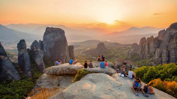 People sit together on a rock formation watching the sunset in Kalabaka, Greece.