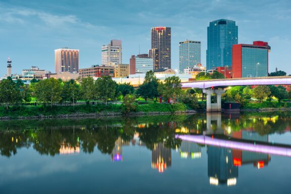 The skyline of Little Rock, Arkansas reflects in the water at twilight.