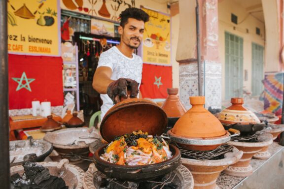 A young man shows off a tagine cooking vegetables in Rissani, Morocco.