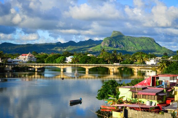 Scenic View of a Riverfront with Bridge, Boats, and Lush Mountains in Mahebourg, Mauritius Mountains can be seen beyond a river in Mahebourg, Mauritius.