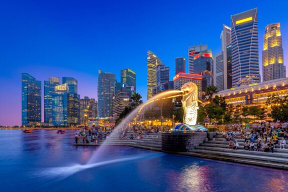 Twilight Cityscape with the Iconic Merlion Fountain in Singapore The Merlion sculpture shoots water into the bay at Merlion Park in Singapore.