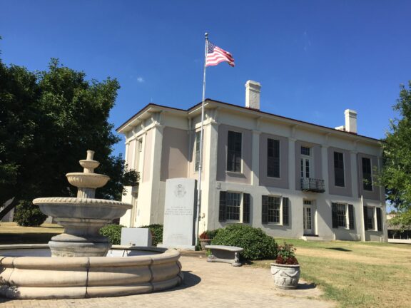 The flag of the United States flies in front of the Greene County Courthouse in Eutaw, Alabama on a sunny day.