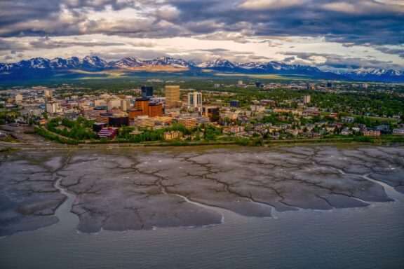 An aerial view of Anchorage with water in the foreground and mountains in the background.