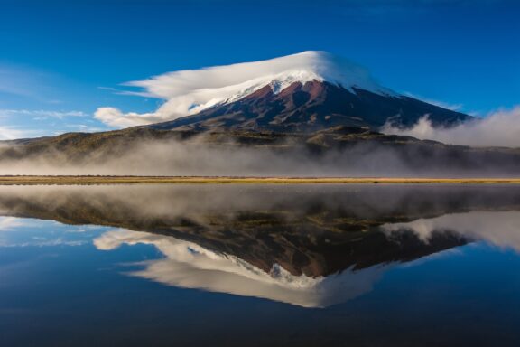 The snow-capped Cotopaxi Volcano's reflection can be seen in a still body of water.