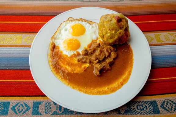 A top-down view of a plate off Bolon de Verde, fried eggs, and meat. 