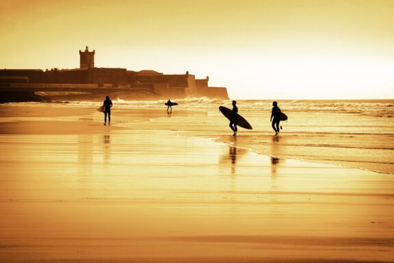 Silhouette of surfers walking in the beach at sunset