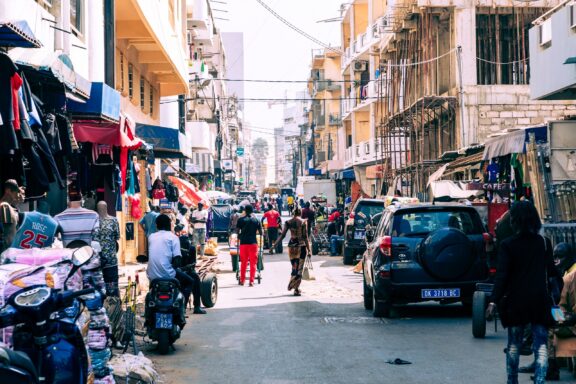 Bustling Street Scene with Locals and Market Stalls Locals commute through the busy streets filled with shops in Daka