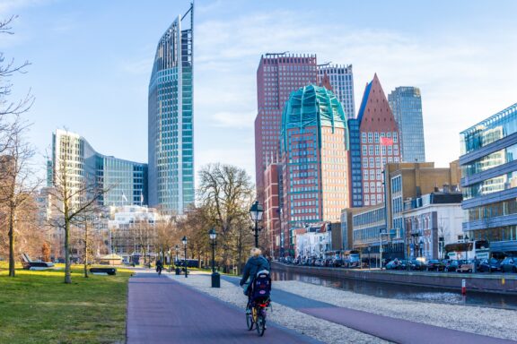 A person rides a bicycle in The Hague, Netherlands with a tall city skyline in the background.