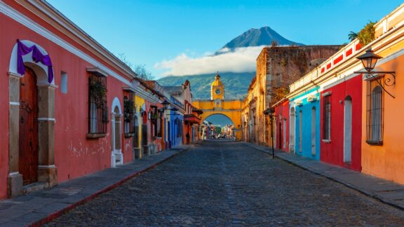 A view of a street in Antigua, Guatemala with a volcano rising in the distance. 