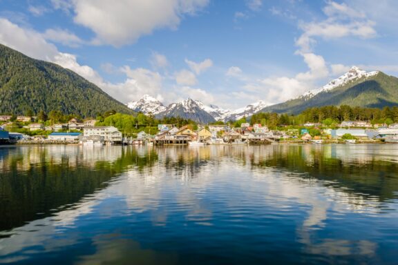 Mountains and buildings reflect in the water on a sunny day in Sitka, Alaska.