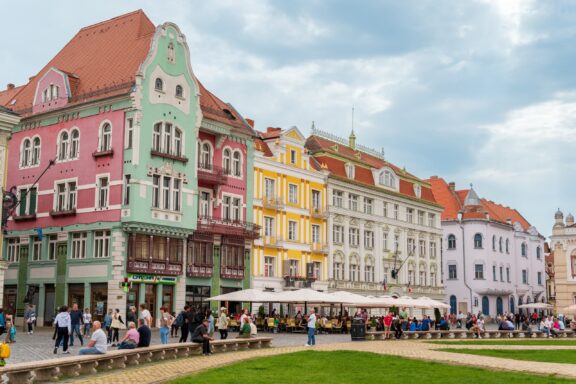 People stand in front of Brück House in Timișoara’s Union Square on a cloudy day. 