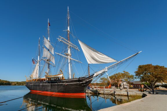 Charles W. Morgan: The Last Wooden Whaleship Docked on a Clear Day The Charles W. Morgan ship sits in the water at the Mystic Seaport in Mystic, Connecticut.