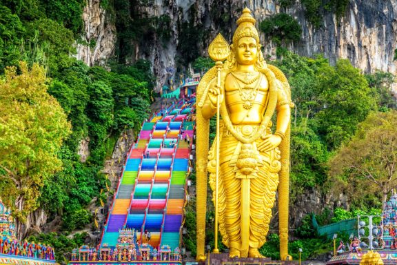 Colorful Stairs and Golden Statue at Batu Caves Entrance The Batu Caves, guarded by a Arulmigu Murugan Golden Statue