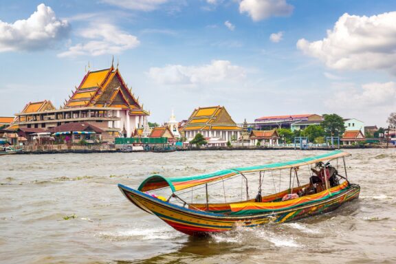 Boat on Chao Phraya River with Thai Temple in Background River Ferry along the Chao Phraya River, a common way for locals and tourists to navigate the city