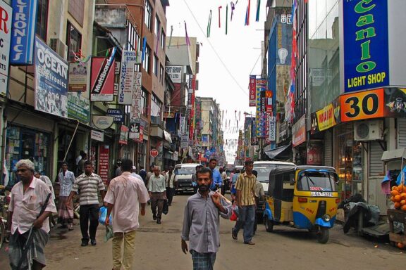 Bustling Street Scene with Shops and Pedestrians Locals commute through market street around Fort Stn & Harbour