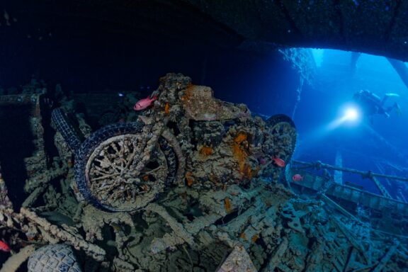 A diver shines a light on a submerged motorcycle at the Thistlegorm shipwreck in the Red Sea.