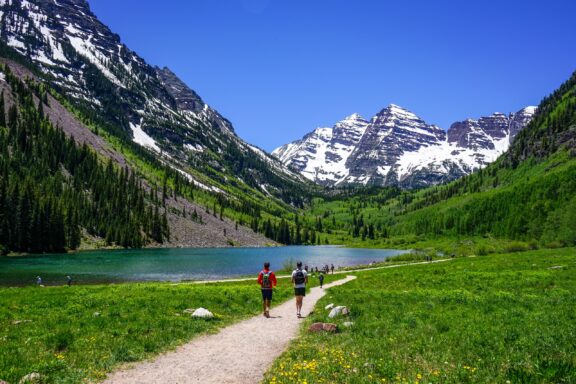 Hikers Walking Towards Maroon Bells in Aspen, Colorado People can be seen jogging near a lake and mountains on a sunny day just outside Aspen, Colorado.