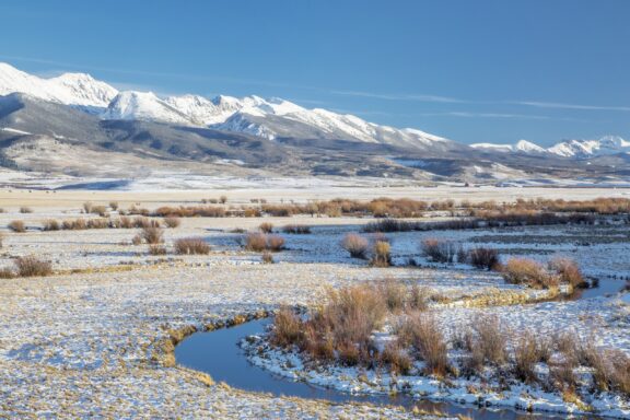 A small river meanders in the foreground, and the Medicine Bow Mountains stand tall in the distance. 