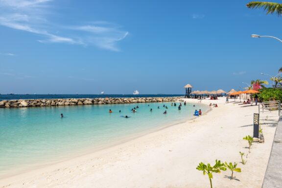 Tropical Beach with Visitors and Clear Blue Sky Rasfannu Beach, popular among both residents and tourists for swimming and watersports