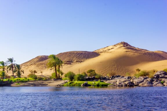 Sand dunes and palm trees line the Nile River in Egypt.