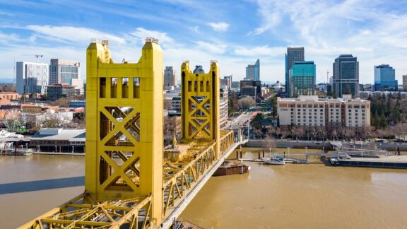 The yellow Tower Bridge stretches across the water in Sacramento, California on a sunny day.