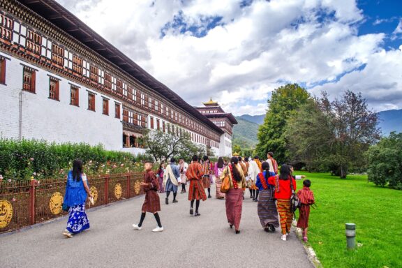Festival Attendees Walking by Traditional Building Locals heading to the Tsechu Festival, a traditional Bhutanese festival celebrated annually