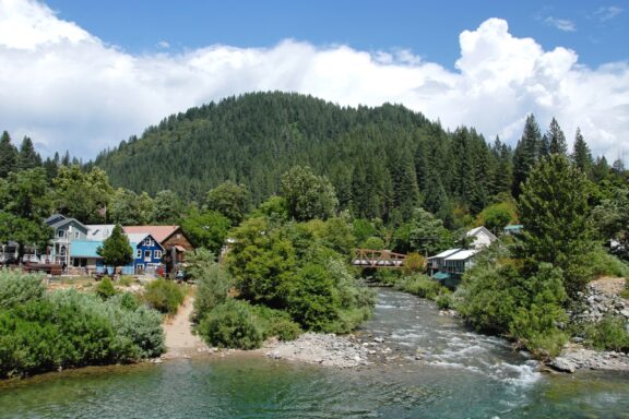 A tree-covered hill sits behind buildings and the Yuba River in Sierra County, California.