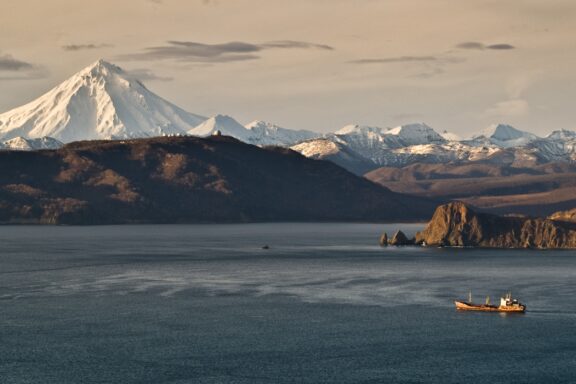 A small ship sails out of Kamchatka Peninsula’s Avacha Bay, and Vilyuchinsk Volcano towers in the distance.