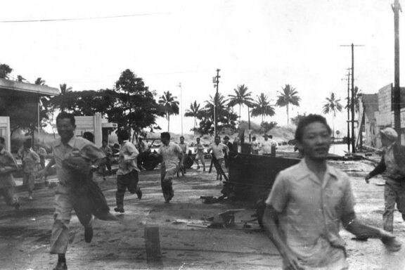 A black-and-white photo shows people running from a tsunami wave in Hilo, Hawaii.