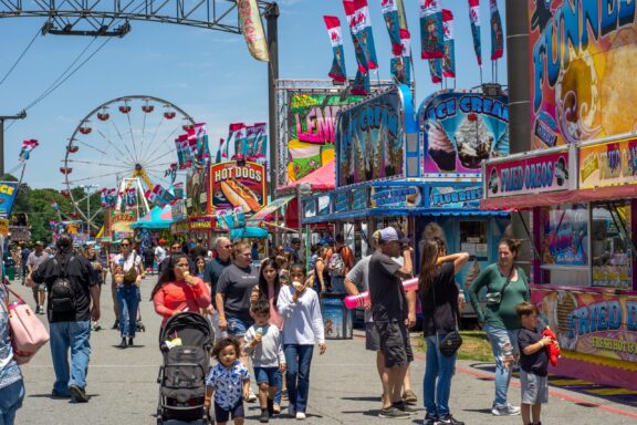 A crowd of people walk through a circus and its colorful signs in Cobb County, Georgia.