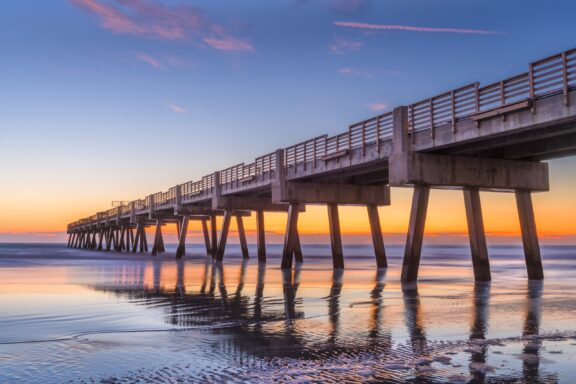 A low-angle view of the Jacksonville Pier extending into the water at sunset.